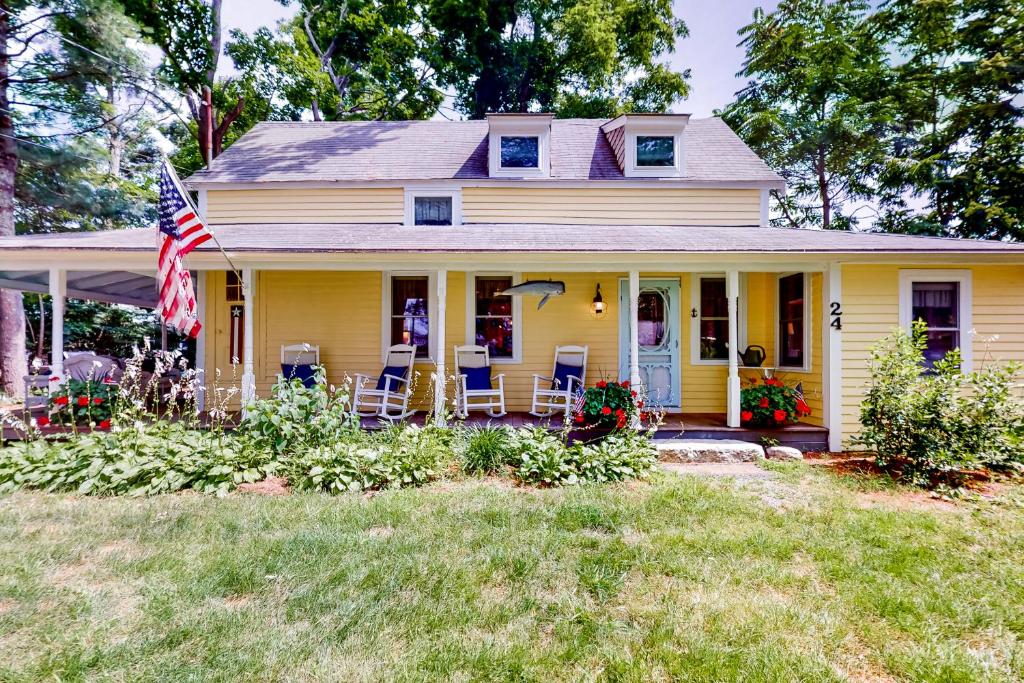 a yellow house with chairs and an american flag at Come About Cottage in Wareham