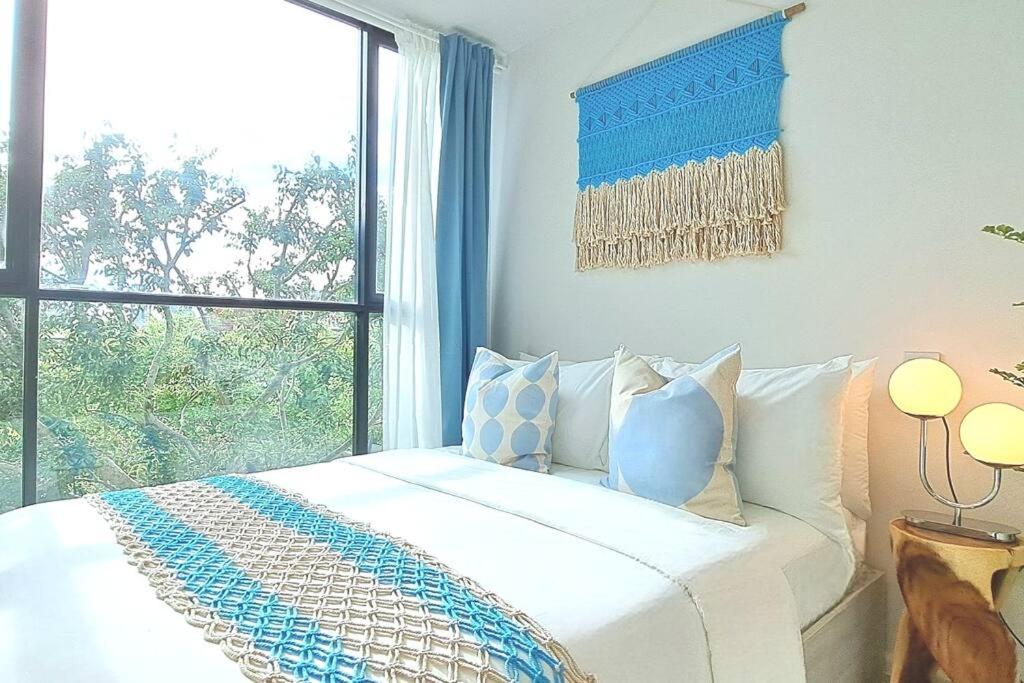 ein weißes Bett mit blauen Kissen in einem Zimmer mit Fenster in der Unterkunft SEA BREEZE VIBE @ ATMOZ BANGNA (Si Iam MRT.) in Ban Khlong Samrong