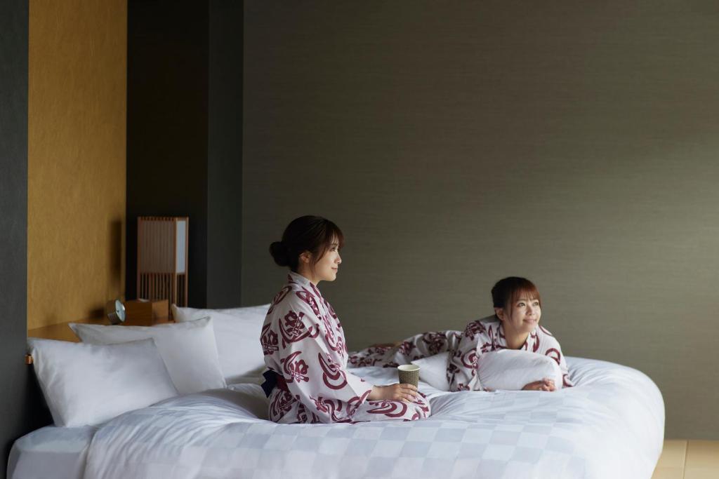 two people in pajamas sitting on a bed at Waqoo Naritasanmonzen in Narita