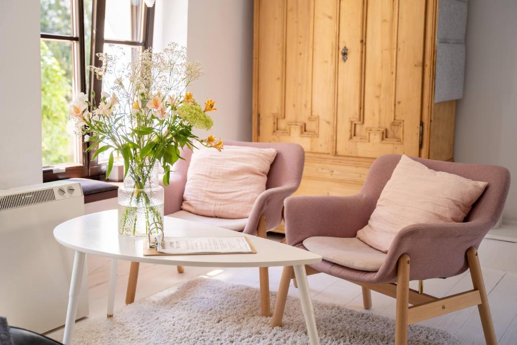 een woonkamer met 2 stoelen en een tafel met een vaas met bloemen bij Tomte - scandinavian apartment in Krakau