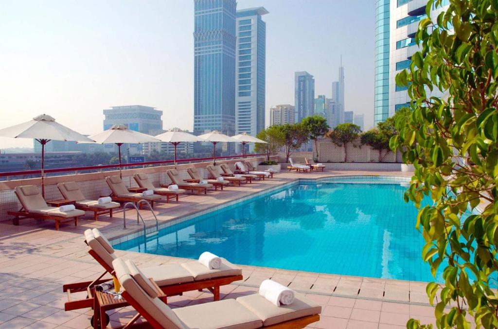 ein Pool mit Stühlen und Sonnenschirmen auf einem Gebäude in der Unterkunft Millennium Plaza Downtown Suites in Dubai