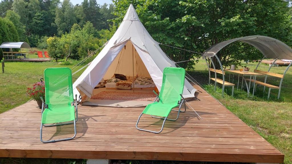 a tent with two green chairs on a wooden deck at Glamping Fluffy Horns - Glempings Pūkainie Ragi in Plieņciems