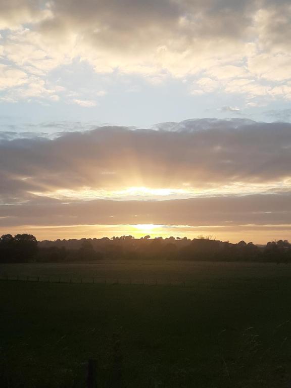 einen Sonnenuntergang auf einem Feld mit Sonnenuntergang am Himmel in der Unterkunft Off grid Rosie Sheperd hut and summerhouse plus 1 acre at Tanyrallt in Llanybyther