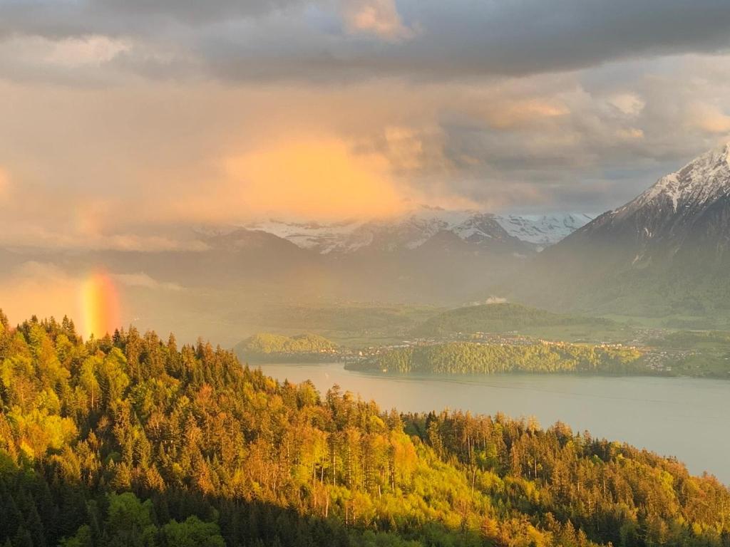 a view of a lake and mountains with a rainbow at Hotel Haltenegg in Heiligenschwendi