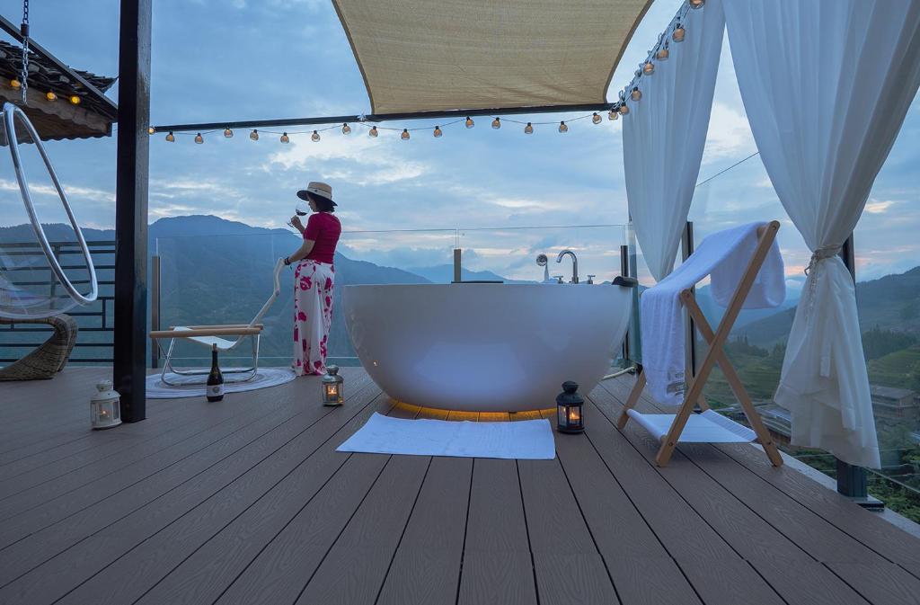 una mujer de pie junto a una bañera en una terraza en Longji One Art Hotel, en Longsheng