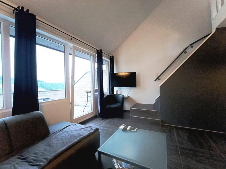 a living room with a couch and a large window at Le Havre du Circuit / Triplex avec Sauna in Malmedy