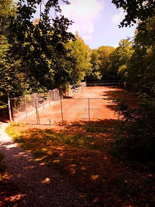 a tennis court with a fence and a dirt field at Le Havre du Circuit / Triplex avec Sauna in Malmedy
