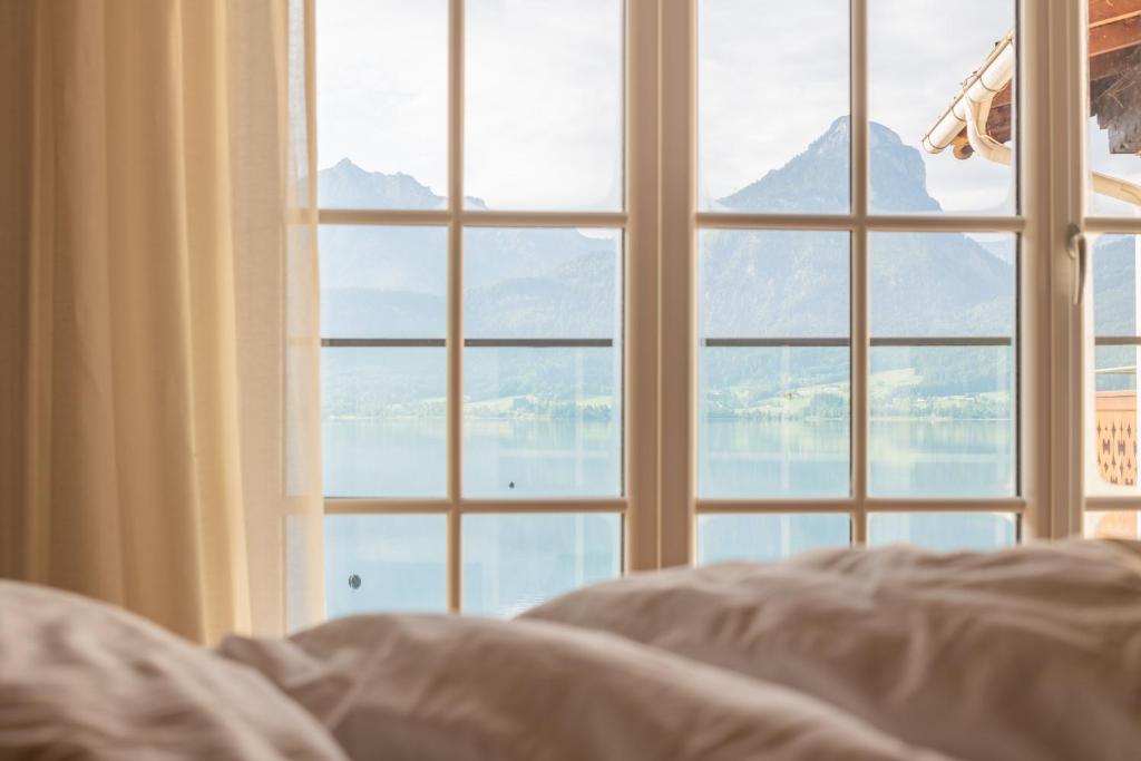 a bed in front of a window looking out at the water at Hotel Seevilla Wolfgangsee in St. Wolfgang