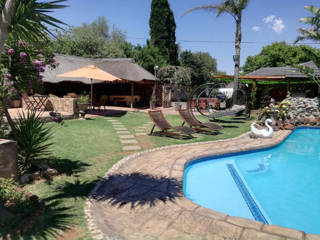 a swimming pool in a yard with chairs and an umbrella at Petra Lodge in Edenvale