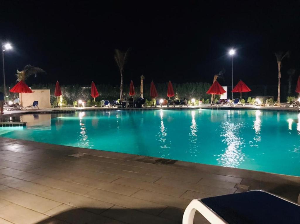 Porto Said Tourist Resort في بورسعيد: مسبح كبير بالليل مع مظلات حمراء