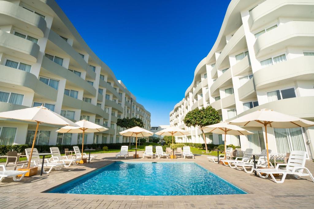 una piscina frente a un edificio con sillas y sombrillas en Casa Andina Select Paracas, en Paracas