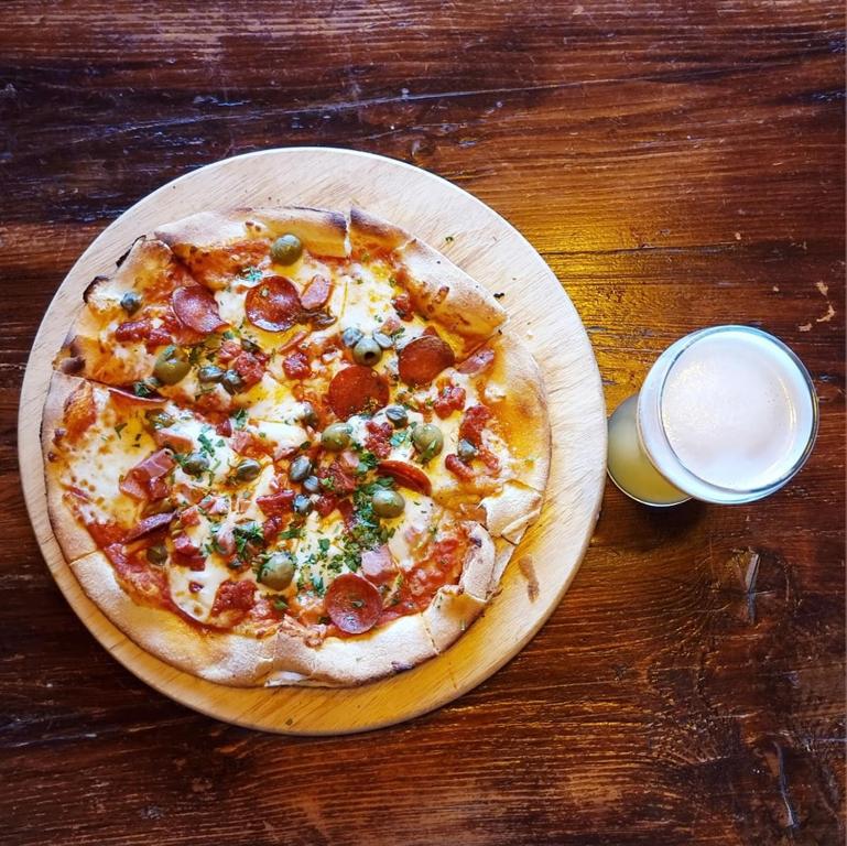 a pizza on a wooden plate on a table with a glass of milk at The Queen Vic Hotel in Monkwearmouth