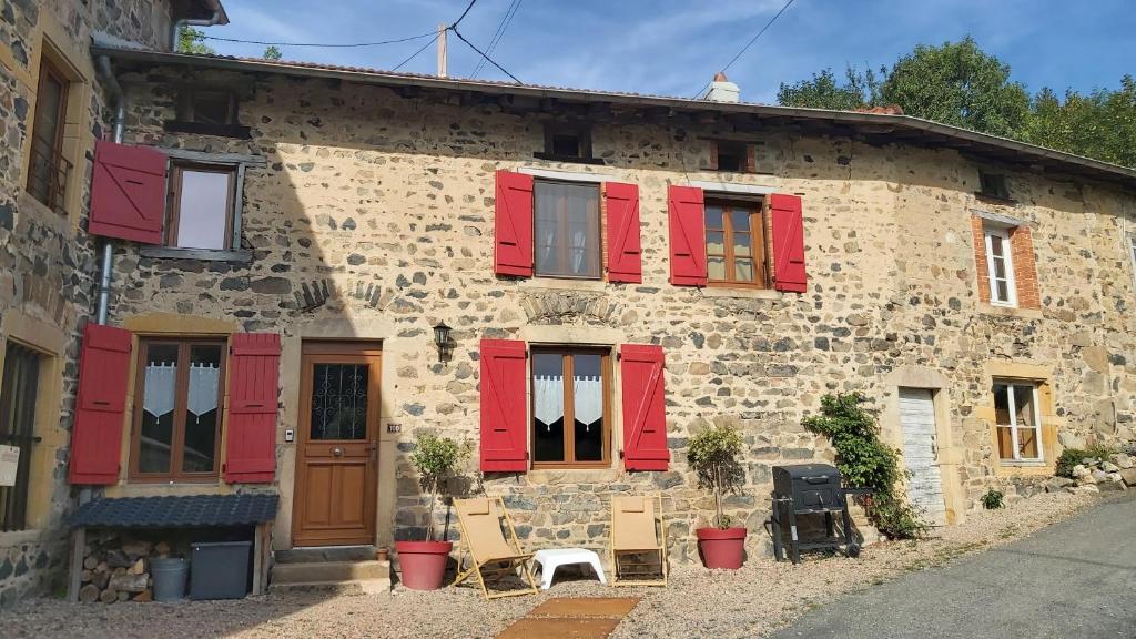 um antigo edifício de pedra com persianas vermelhas e cadeiras em Gîte du moulin em Chénelette