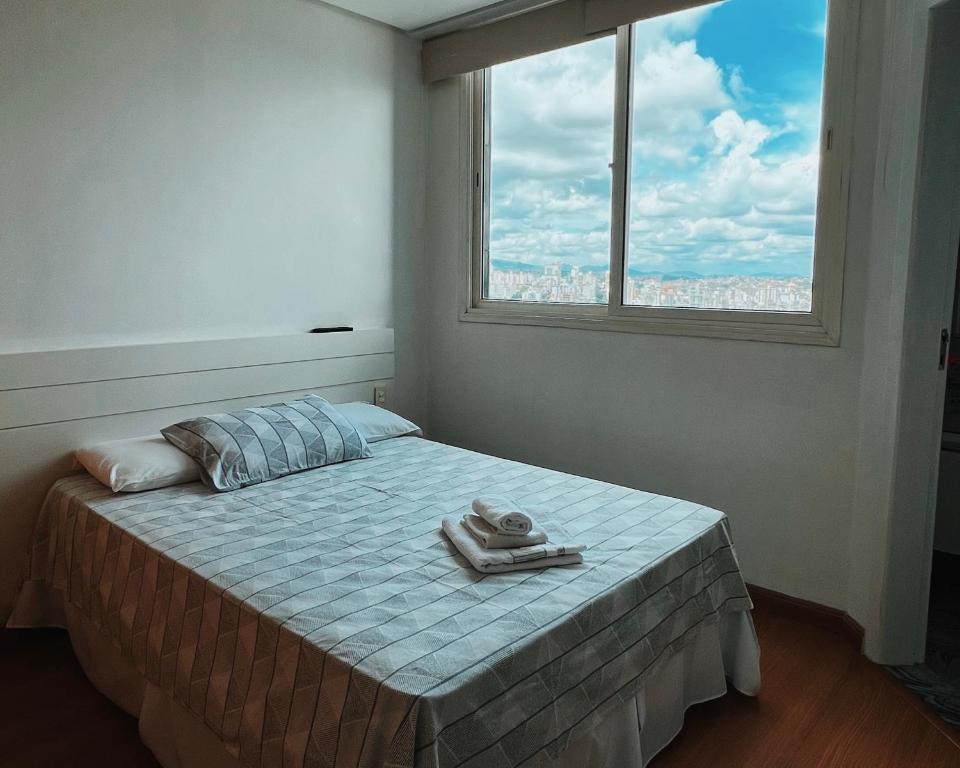 1 dormitorio con 1 cama con ventana y toalla en BH PARA 2 - STUDIO - Estoril, en Belo Horizonte