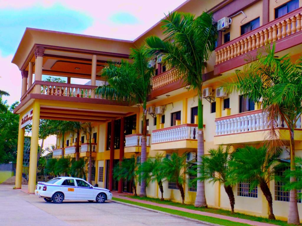 a white car parked in front of a building with palm trees at Hotel Las Hamacas in La Ceiba