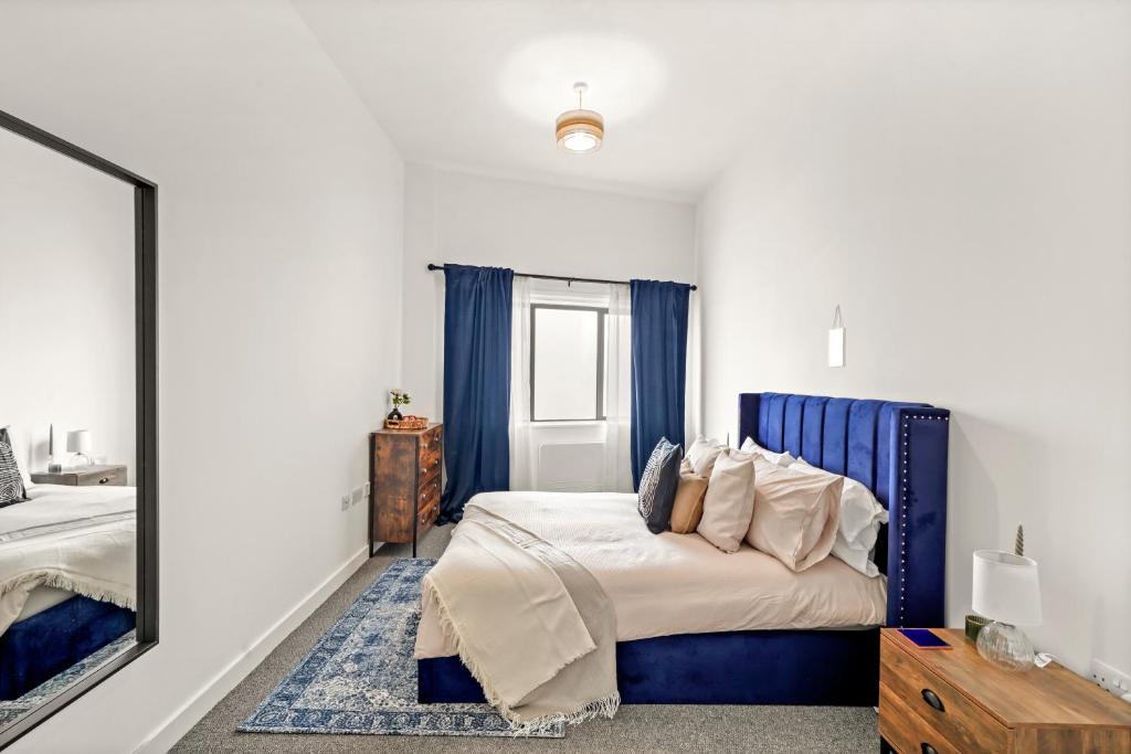 1 dormitorio con 1 cama con cabecero azul y espejo en Luxury London Canary Wharf 2 bed apt, en Londres