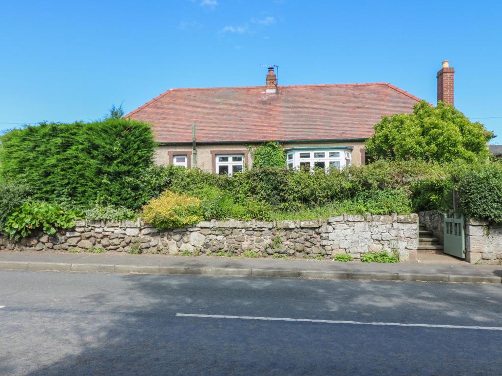 a house with a stone wall next to a street at Charlies Cottage in Duns