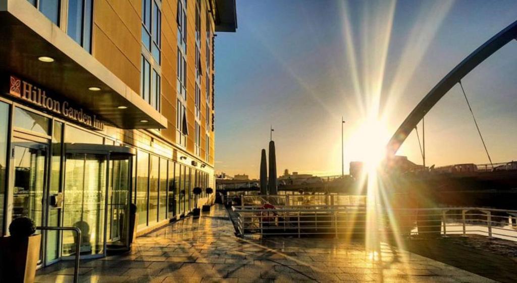 a sun setting behind a building in a city at Hilton Garden Inn Glasgow City Centre in Glasgow