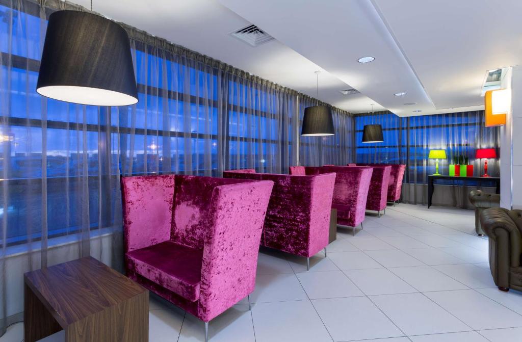 a row of purple chairs in a room with windows at Hampton by Hilton Liverpool John Lennon Airport in Speke