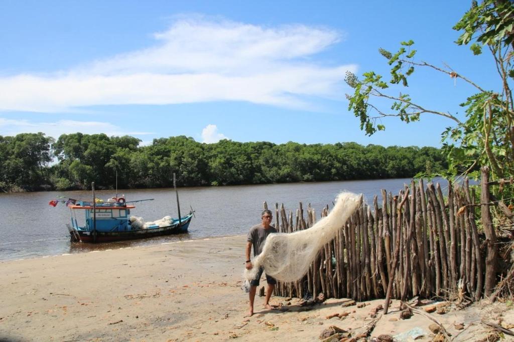 a man standing on a beach next to a boat at Rancho Dias in Atins