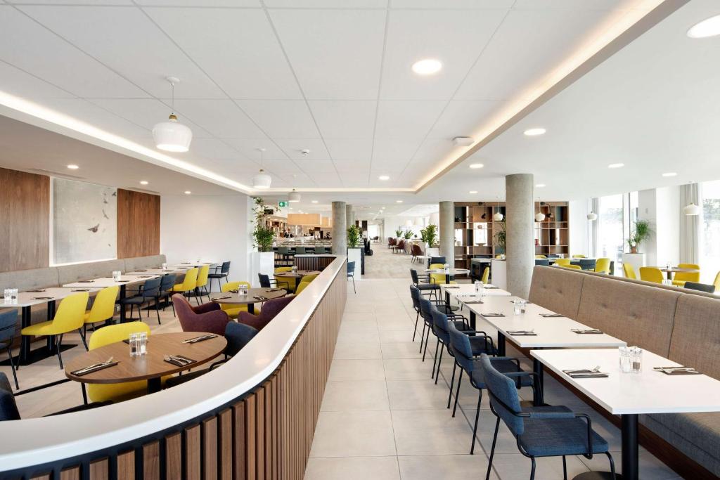 a dining room with tables and yellow chairs at Hampton By Hilton London Stansted Airport in Stansted Mountfitchet