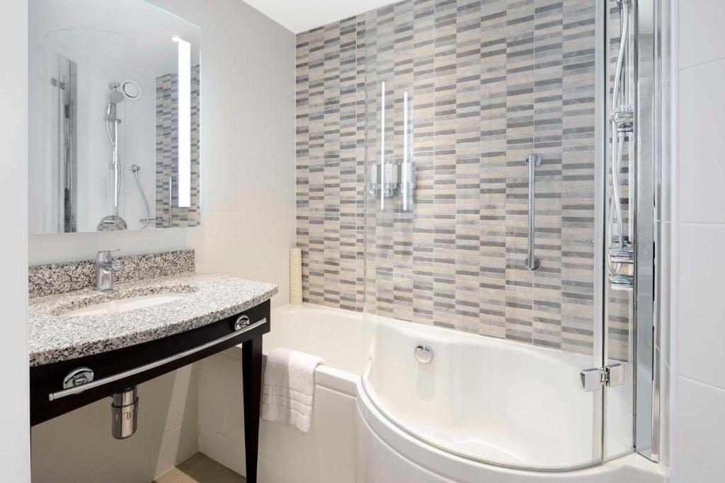 a bathroom with a tub and a sink and a shower at Hampton By Hilton London Stansted Airport in Stansted Mountfitchet