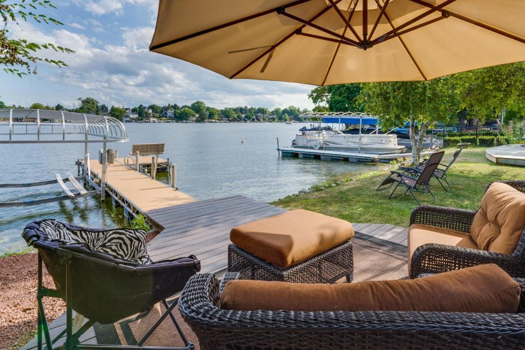 a patio with chairs and an umbrella next to the water at Okauchee Lake Vacation Rental with Boat Dock! in Oconomowoc