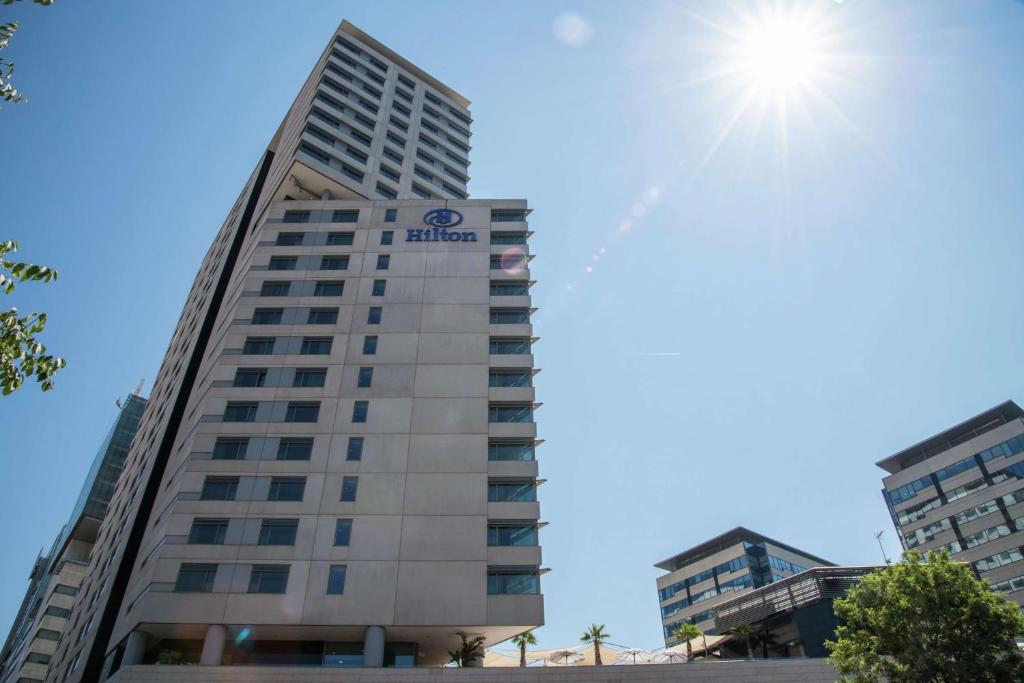 a tall building with the sun in the sky at Hilton Diagonal Mar Barcelona in Barcelona