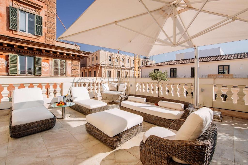 un patio con mobili bianchi e ombrellone di Aleph Rome Hotel, Curio Collection By Hilton a Roma