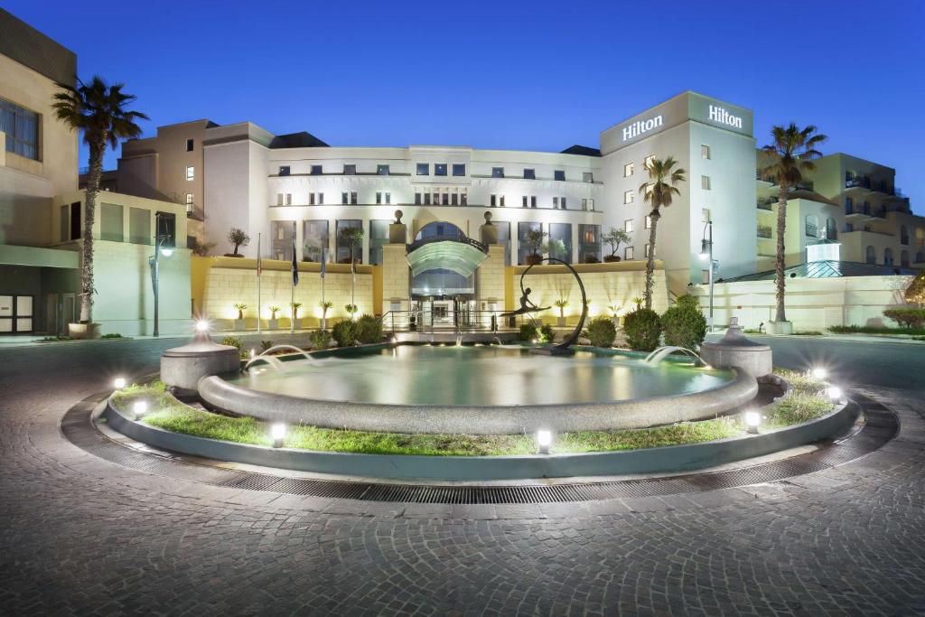 un grand bâtiment avec une fontaine devant lui dans l'établissement Hilton Malta, à San Ġiljan
