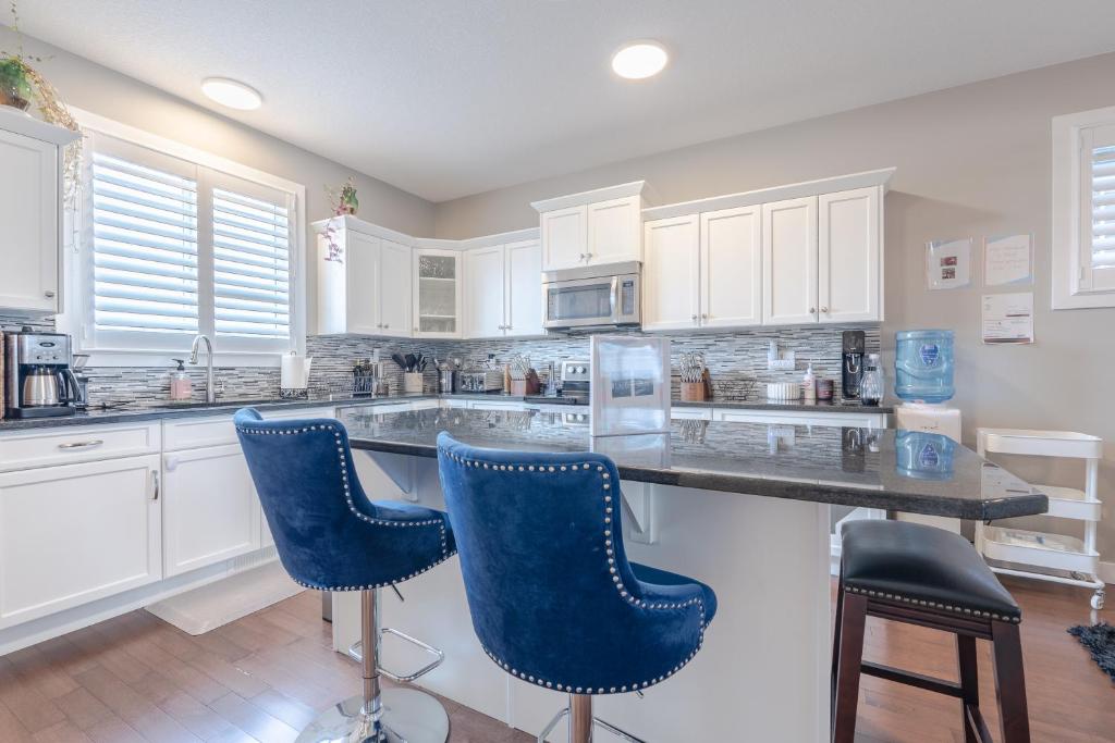 a kitchen with white cabinets and blue bar stools at Luxurious 3-Bedrooms with Office & Media Room in Cochrane
