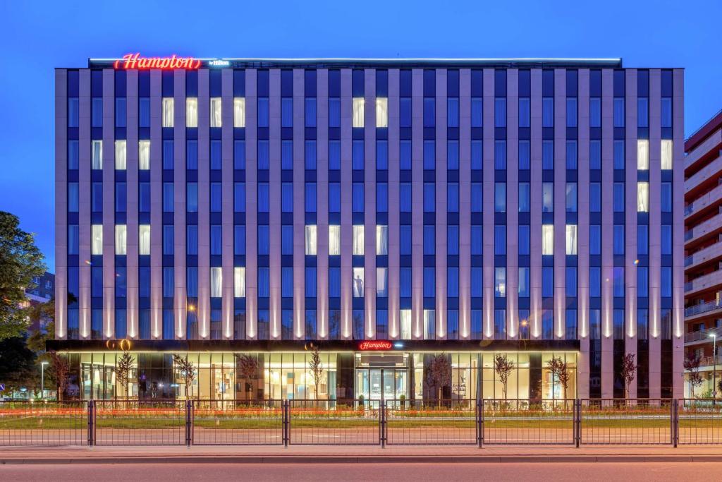 un grand bâtiment avec des fenêtres bleues devant lui dans l'établissement Hampton By Hilton Warsaw Mokotow, à Varsovie