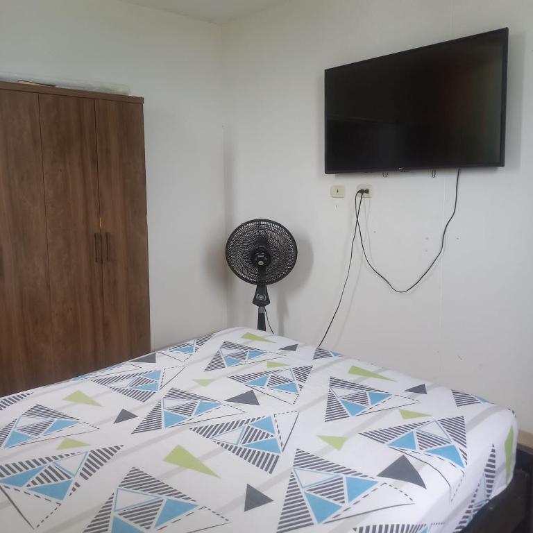 a bed with a comforter with a television on a wall at Habitacion valledupar in Valledupar