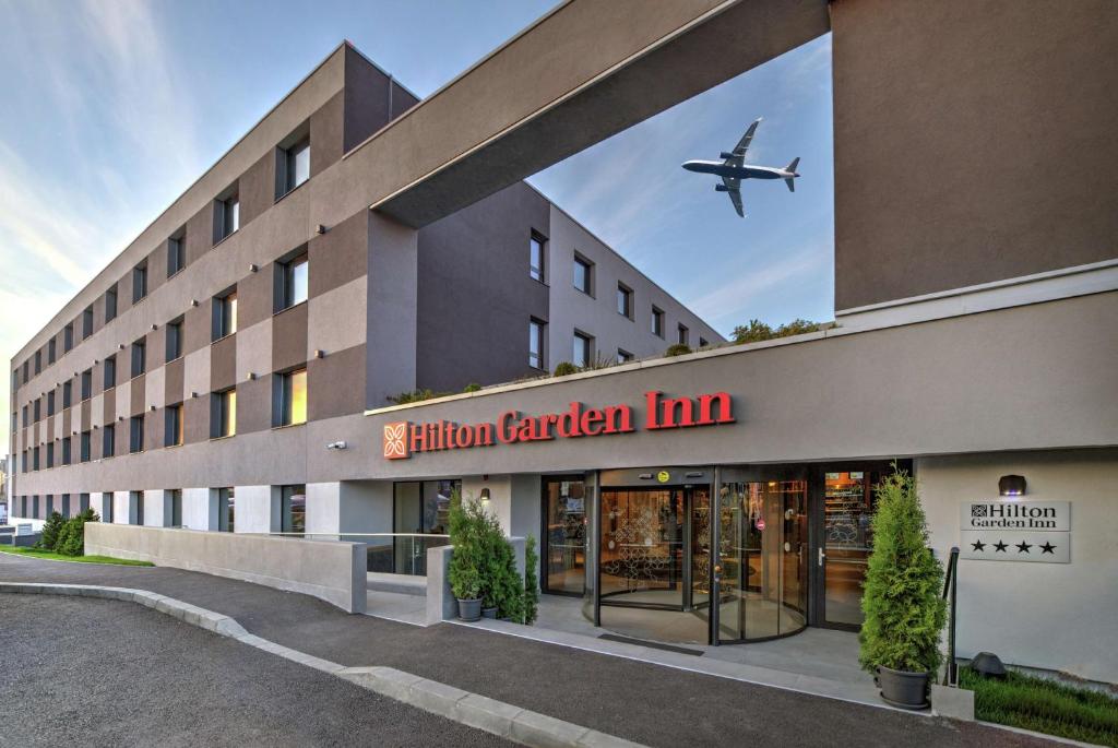 an airplane is flying over a hotel with a building at Hilton Garden Inn Bucharest Airport in Otopeni