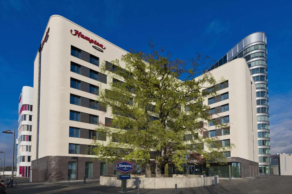 un edificio con un albero di fronte di Hampton By Hilton Frankfurt Airport a Francoforte sul Meno
