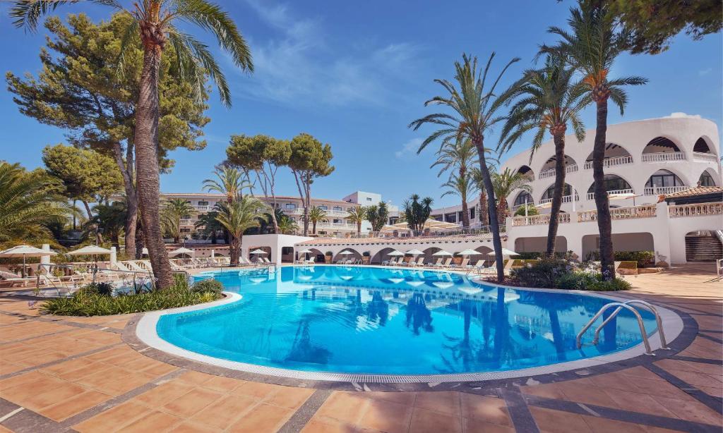 una piscina en el patio de un complejo con palmeras en Hilton Mallorca Galatzo en Paguera