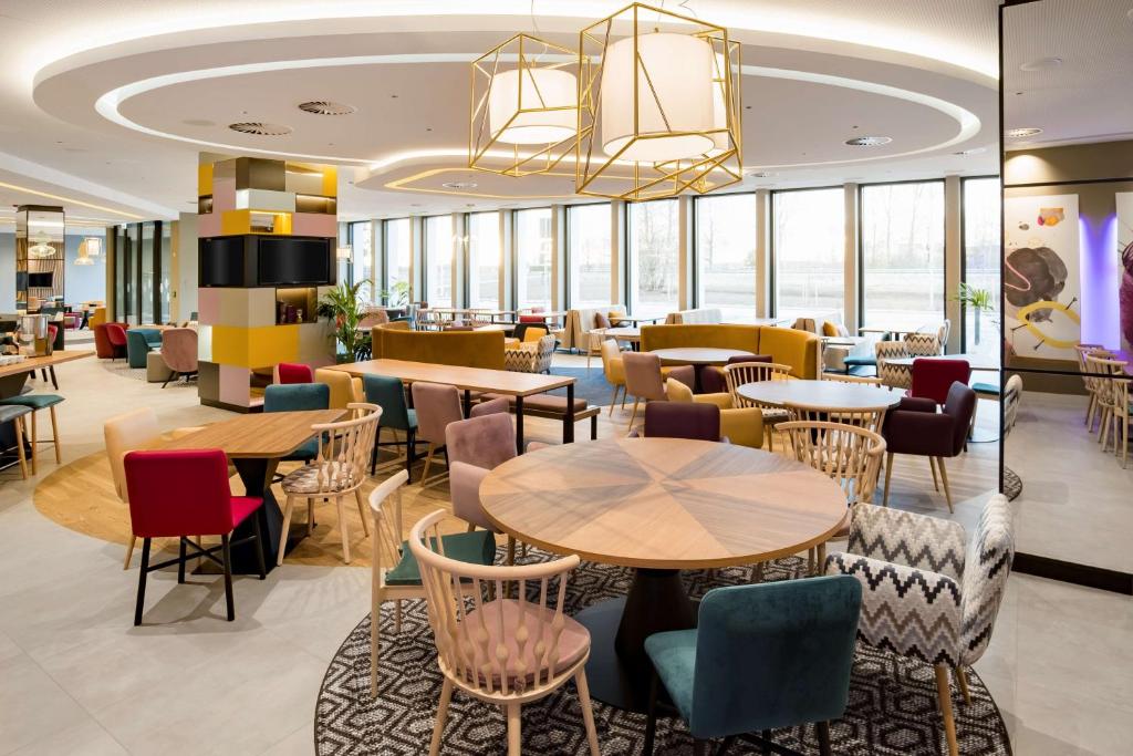 a restaurant with tables and chairs and windows at Hampton by Hilton Riga Airport in Riga