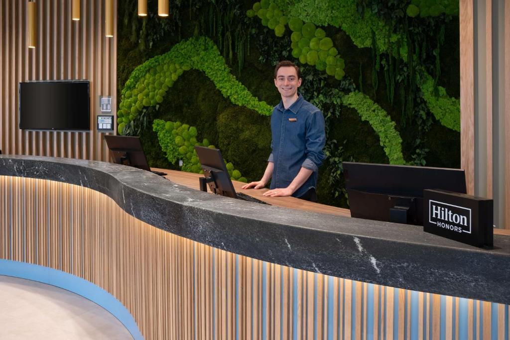 a man sitting in front of a counter with two laptops at Hampton by Hilton Riga Airport in Riga