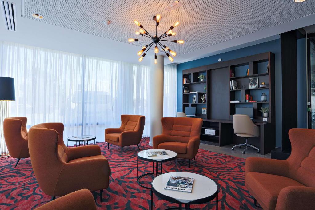 a waiting room with chairs and tables and a chandelier at Hampton By Hilton Toulouse Airport in Blagnac