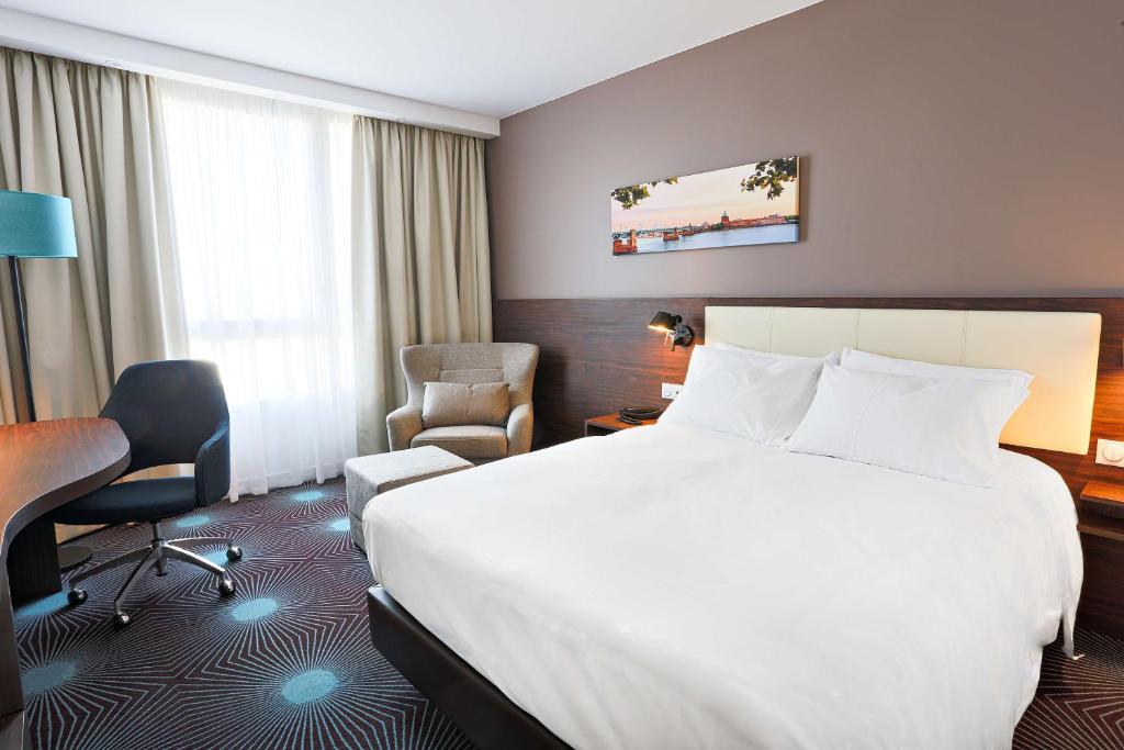 a hotel room with a bed and a desk and chair at Hampton By Hilton Toulouse Airport in Blagnac