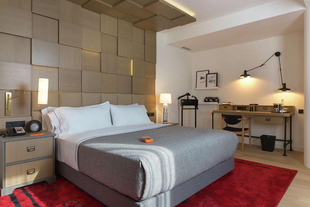 King bed with textured wood headboard, bedside lamps, wall reading light, desk with kettle and safe, red area rug at Canopy by Hilton Zagreb City Centre in Zagreb