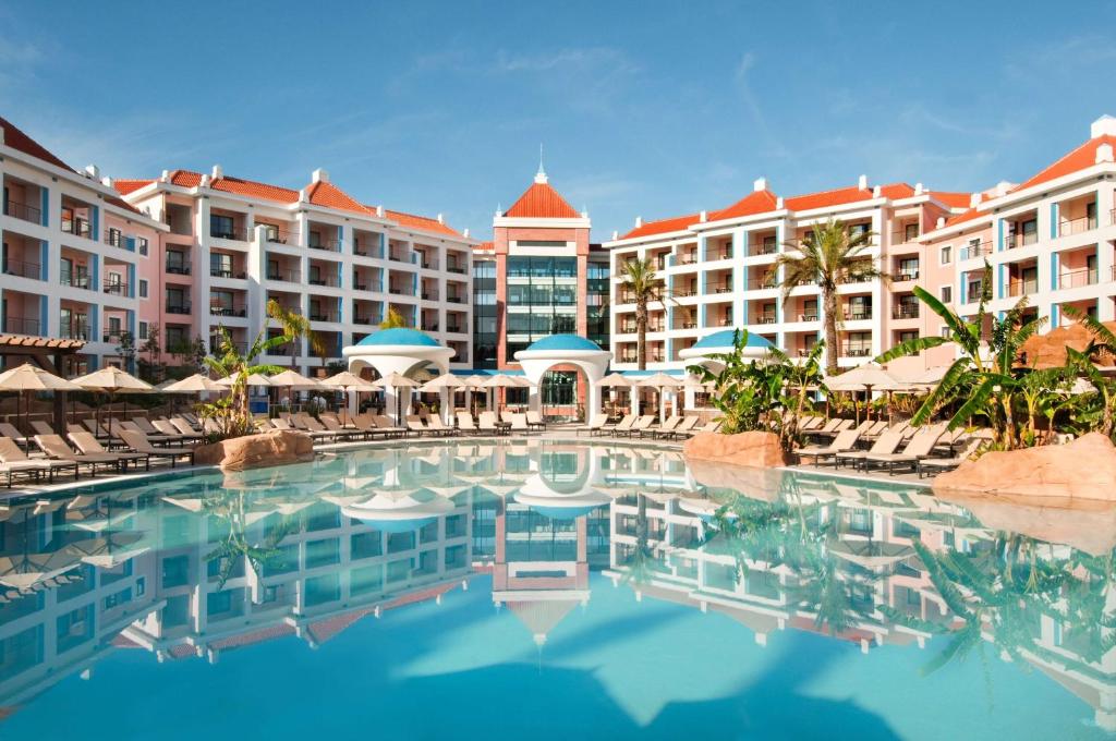 a pool at a resort with chairs and buildings at Hilton Vilamoura in Vilamoura
