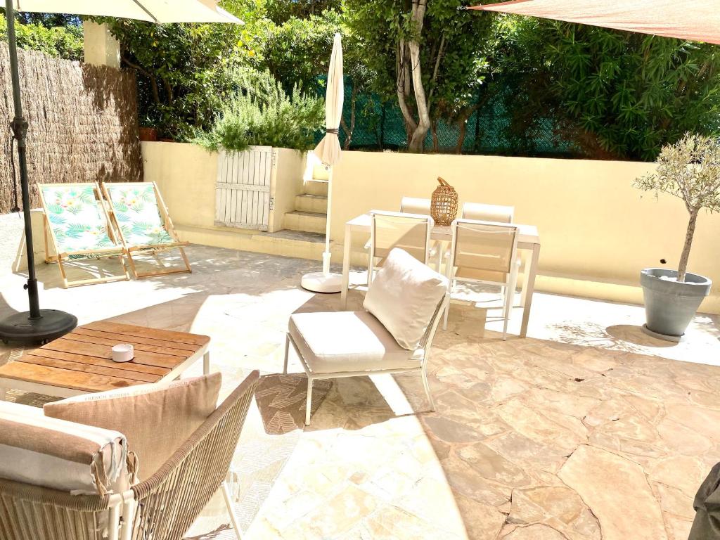 um pátio com cadeiras, uma mesa e um guarda-sol em Appartement 3P 88 m2 terrasse et jardin à 20 metres de la plage em Antibes