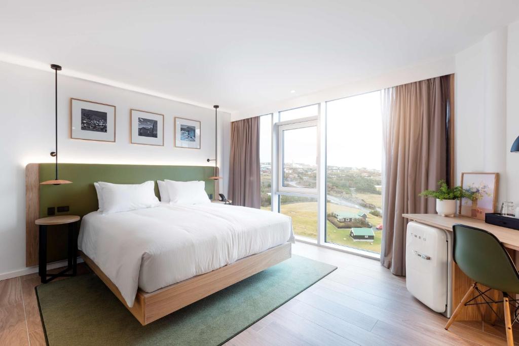een slaapkamer met een bed, een bureau en een groot raam bij Hilton Garden Inn Faroe Islands in Tórshavn