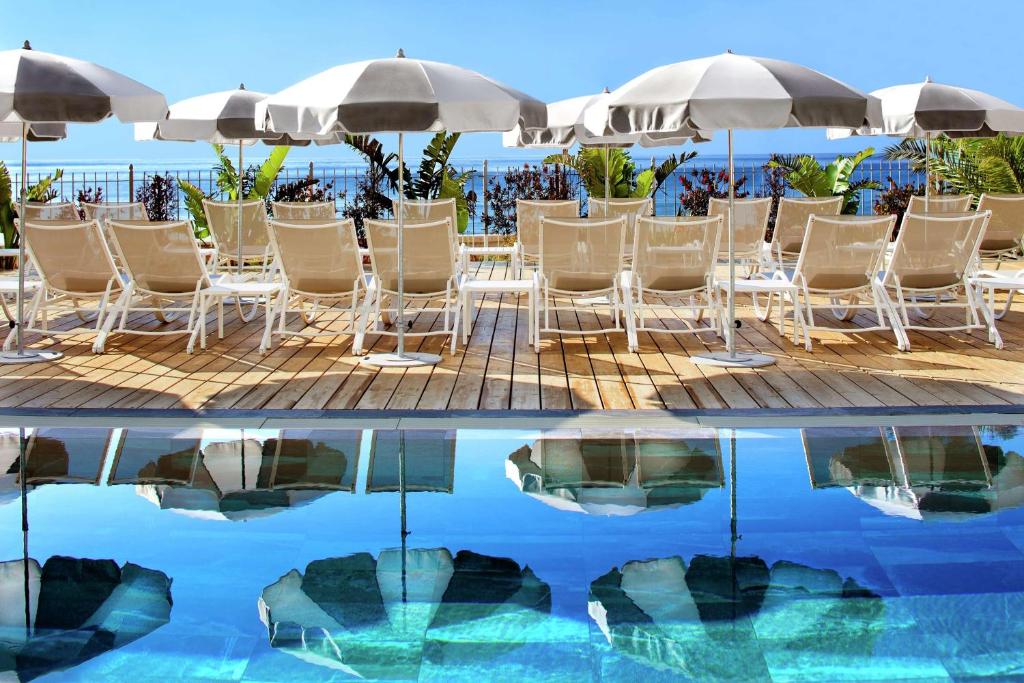 a group of chairs and umbrellas next to a pool at Grand Hotel Des Sablettes Plage, Curio Collection By Hilton in La Seyne-sur-Mer