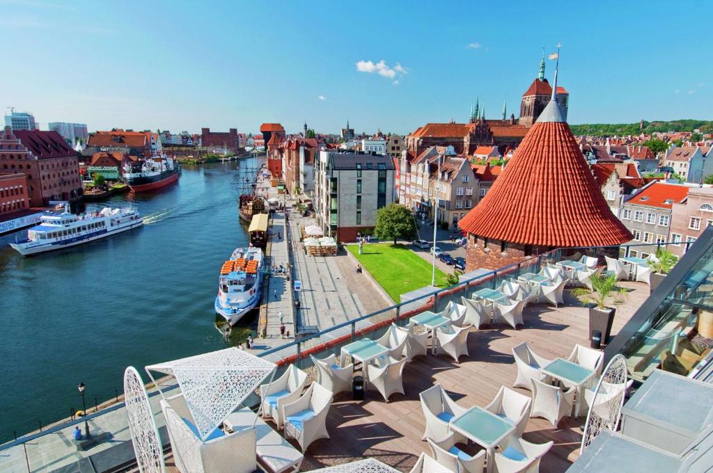 Blick auf einen Fluss mit Stühlen und eine Stadt in der Unterkunft Hilton Gdansk in Danzig