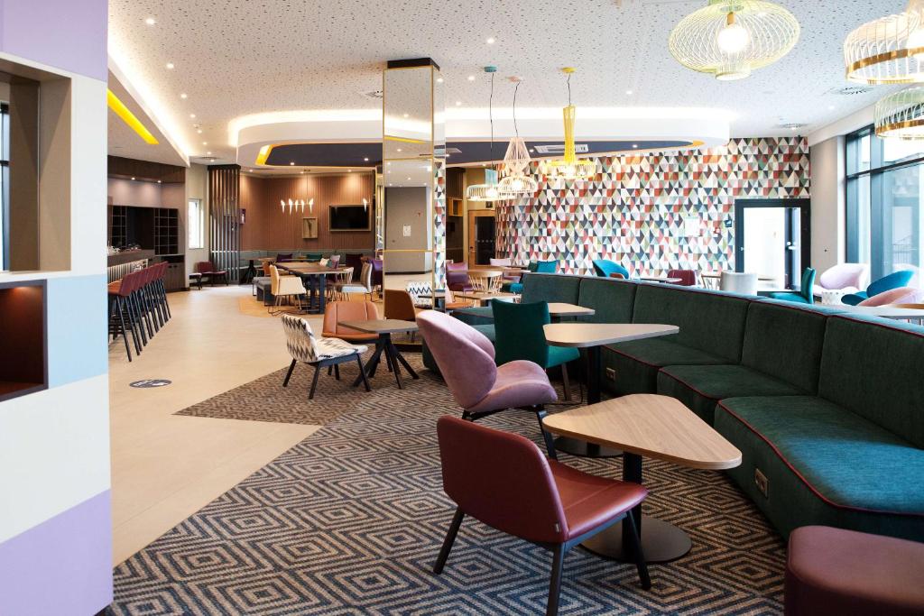 un restaurante con un sofá verde, mesas y sillas en Hampton by Hilton Munich Airport South, en Hallbergmoos