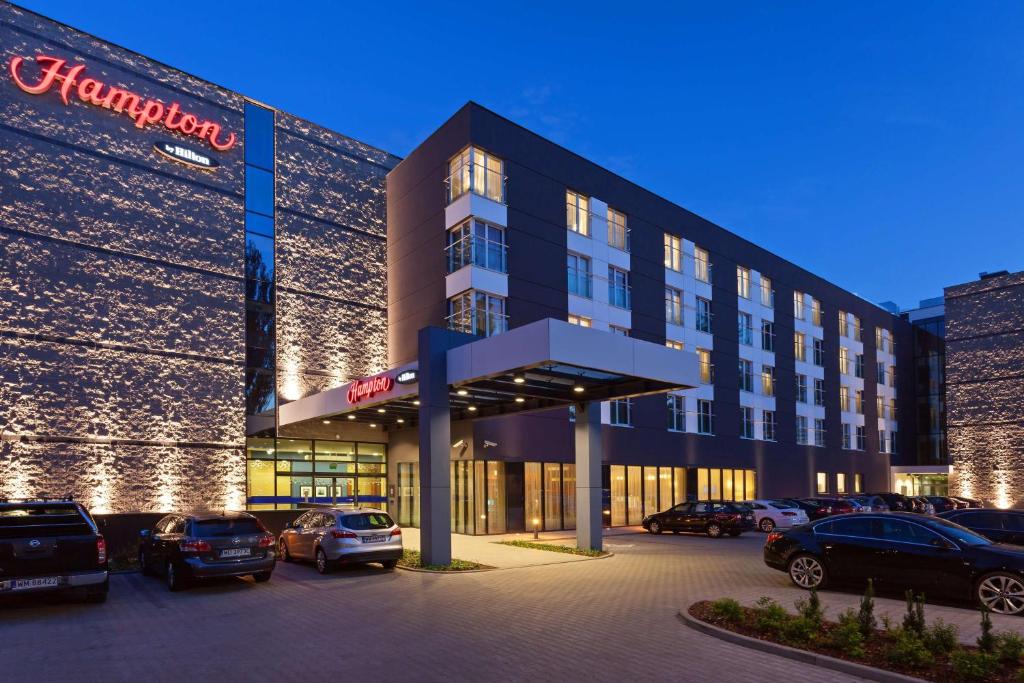 un gran edificio con coches estacionados en un estacionamiento en Hampton by Hilton Warsaw Airport, en Varsovia