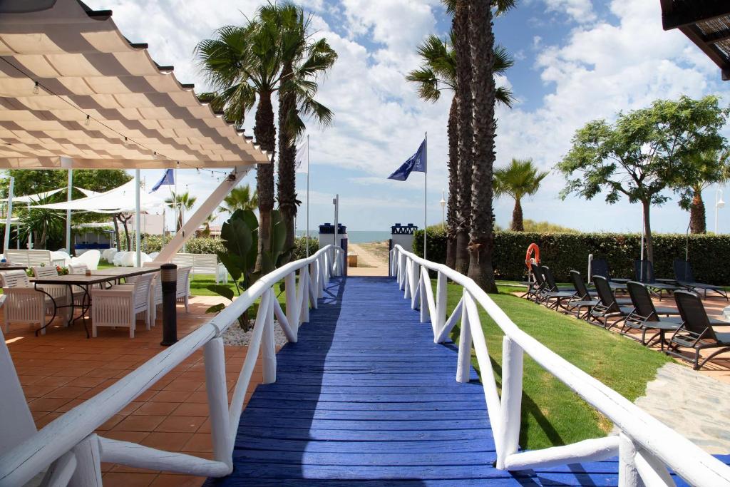 a wooden walkway leading to a beach with palm trees at DoubleTree by Hilton Islantilla Beach Golf Resort in Islantilla