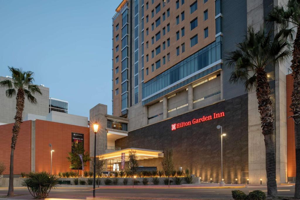 Hilton Garden Inn Chihuahua في تشيواوا: مبنى كبير أمامه أشجار نخيل